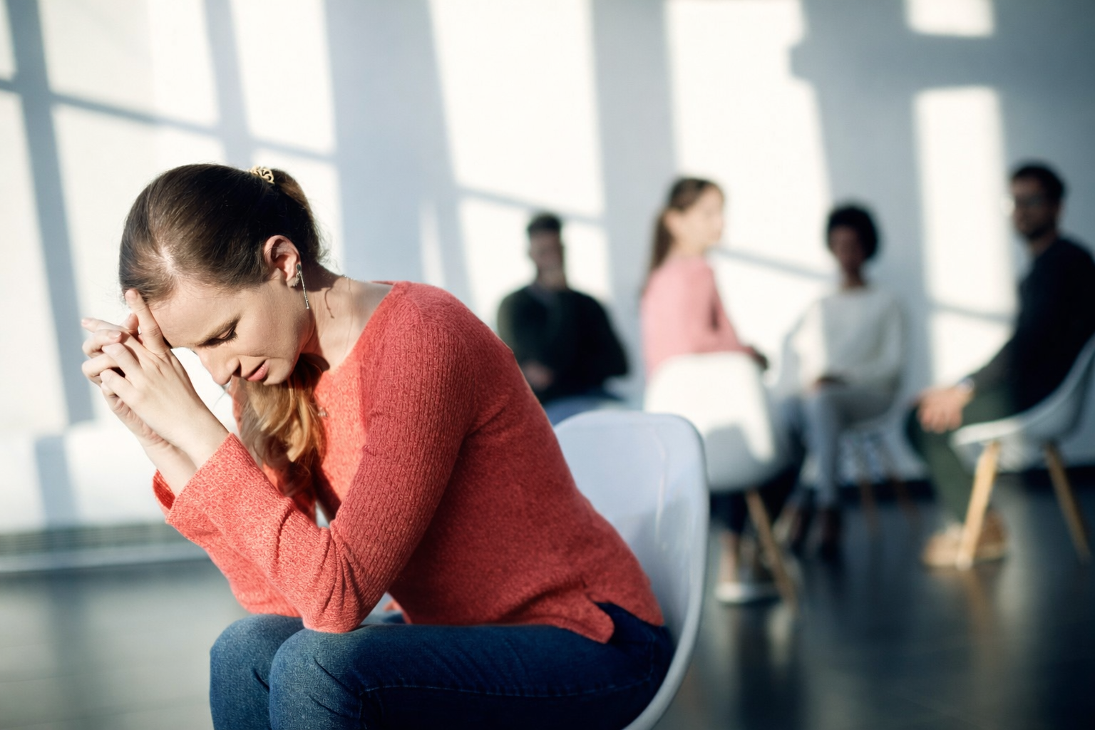 Woman sitting in a therapy group appearing distressed, representing social anxiety and trauma recovery through hypnotherapy in Greenwich London.